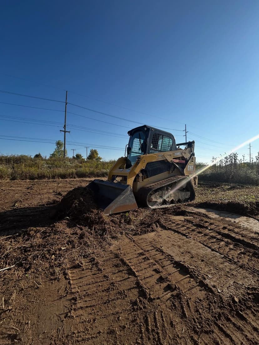 Caterpillar skid steer loader leveling ground on construction site under blue sky.